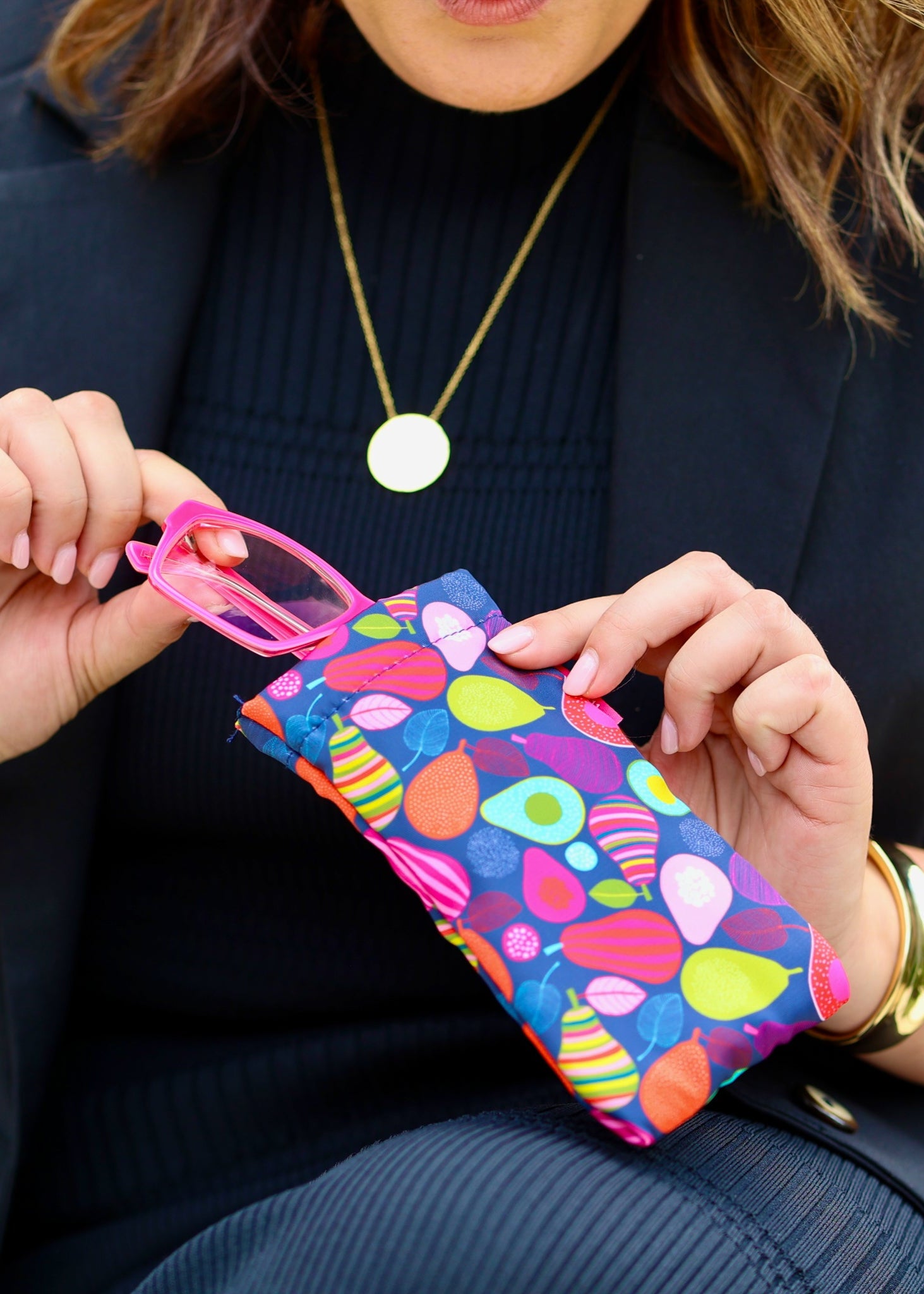 A person holding a multicolored glasses case with a pear design.