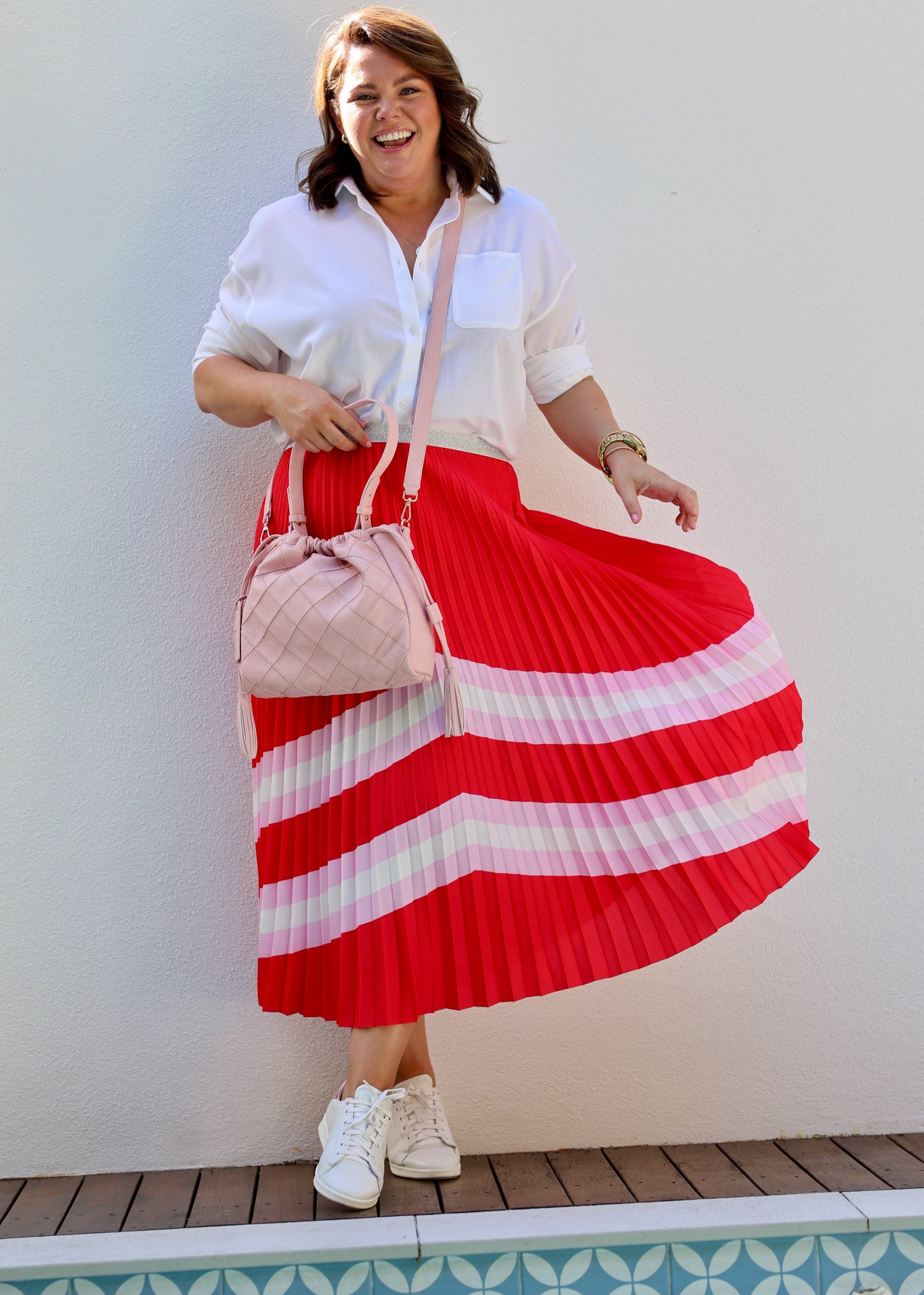 Woman in a white shirt and red and white striped skirt standing by a pool.