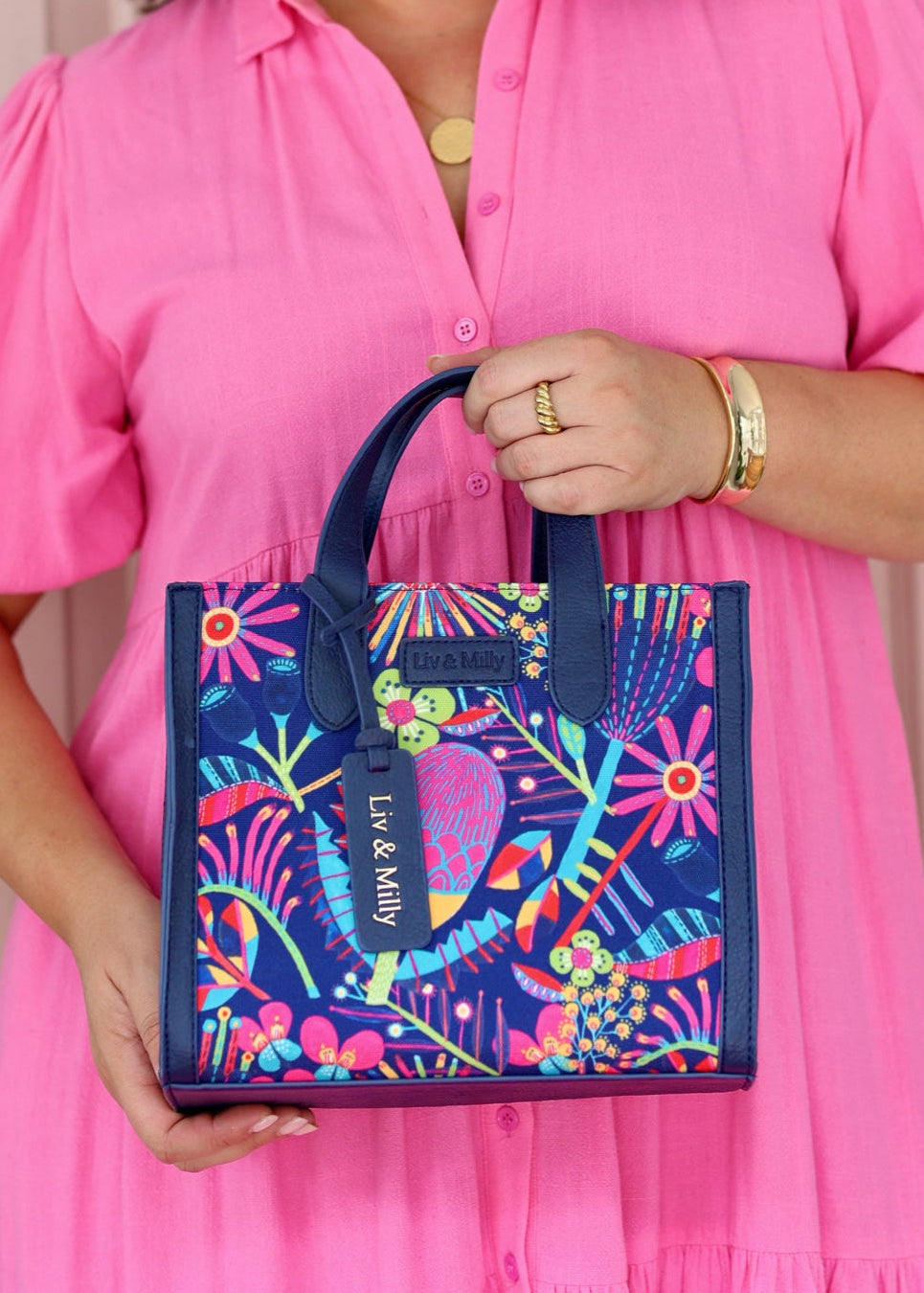 A person in a pink dress holding a multicolored canvas tote bag with a 'Wildflowers' print and navy vegan leather trim.