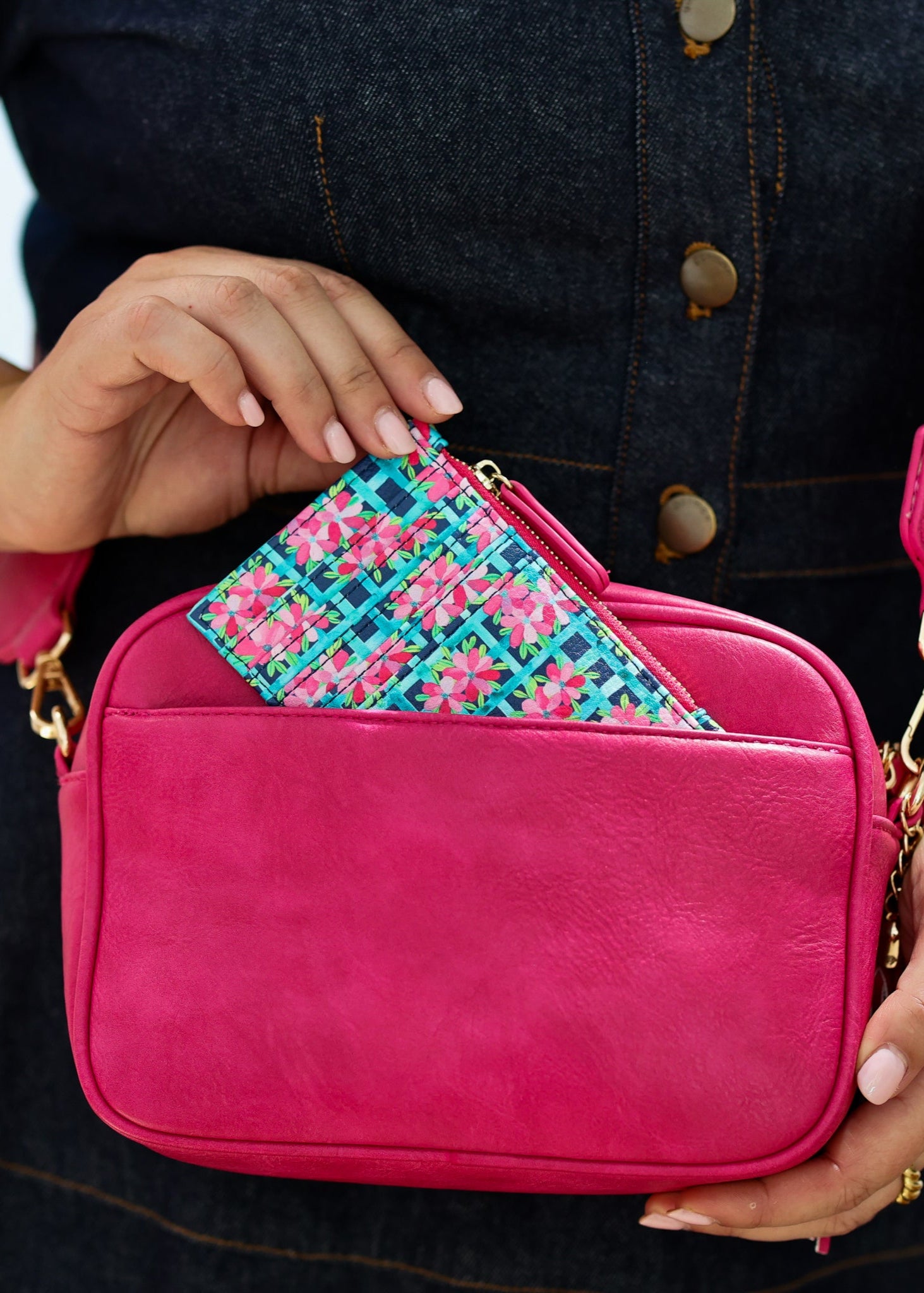 A person holding a bright pink card wallet with a 'Garden Trellis' pattern and vegan leather material. The wallet is attached to a bag with a patterned strap.