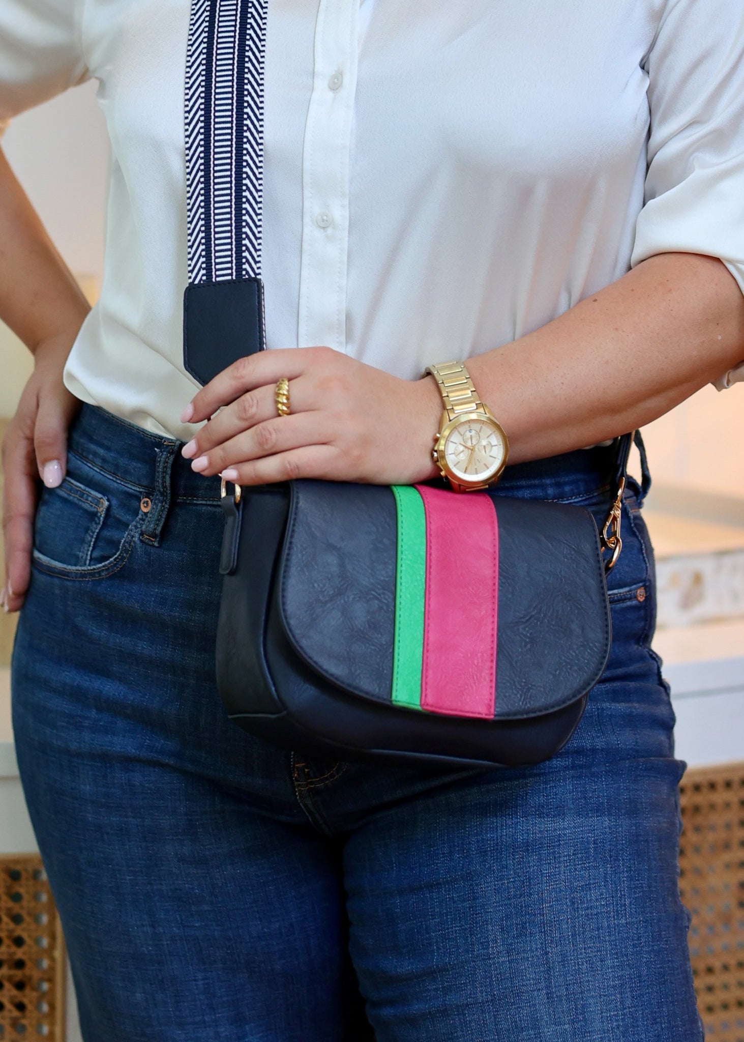 Person wearing a navy blue bag with colorful stripes, white shirt, and gold watch.