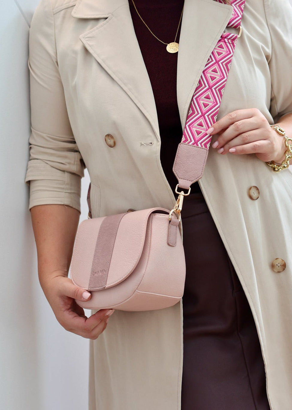 A person wearing a pastel pink/pastel purple crossbody bag with a soft vegan leather finish and a patterned guitar strap, paired with a beige coat.