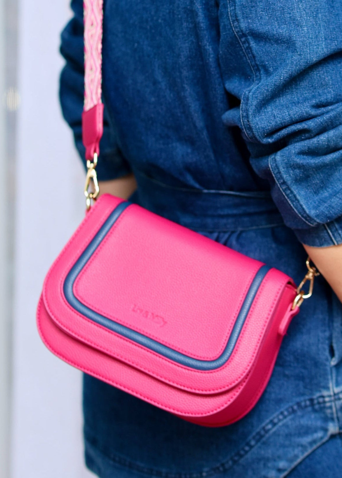A person wearing a blue denim jacket is carrying a pink crossbody bag with a chain strap.